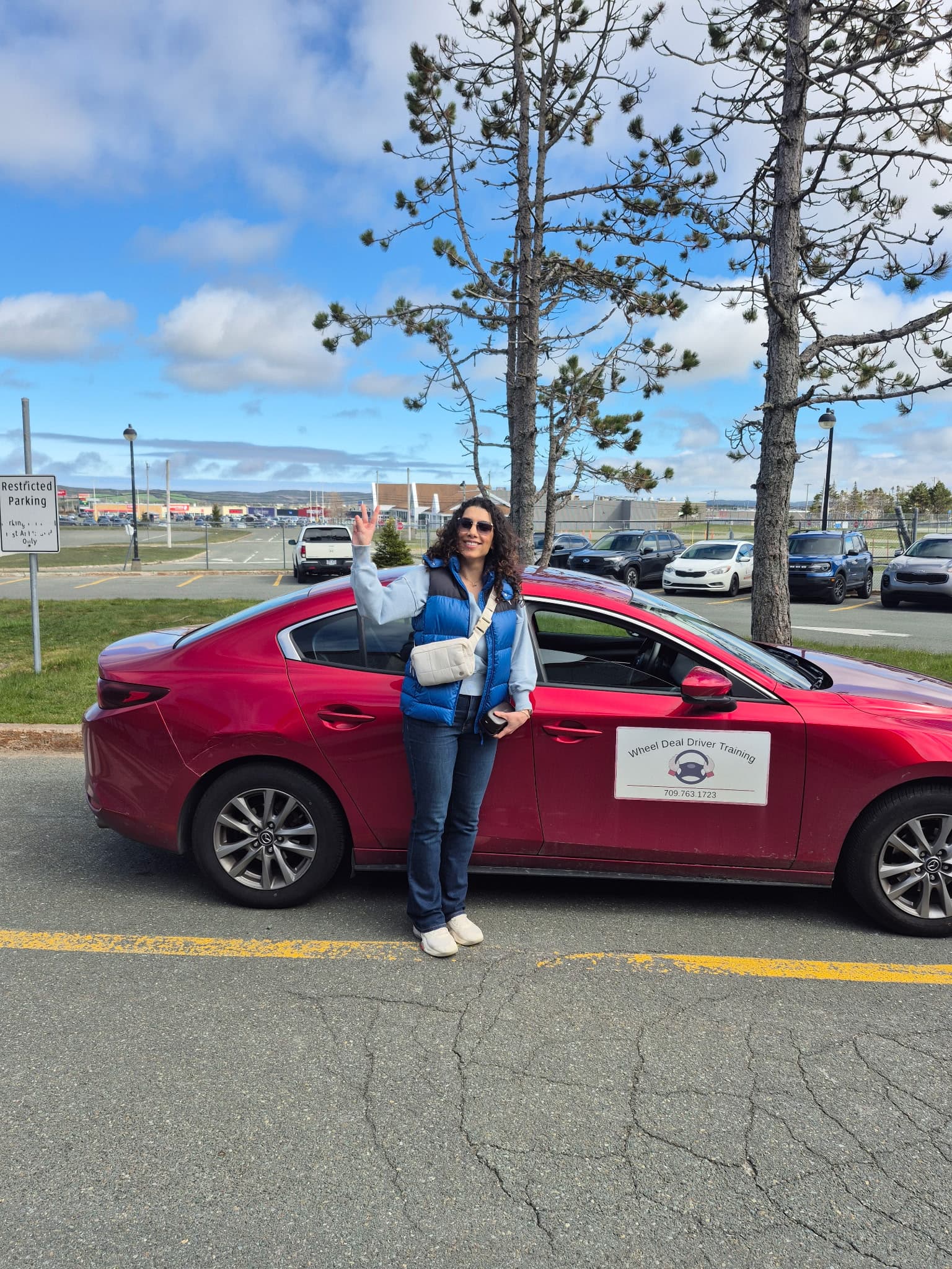 A happy Wheel Deal student giving a peace sign beside the red training car on a sunny day
